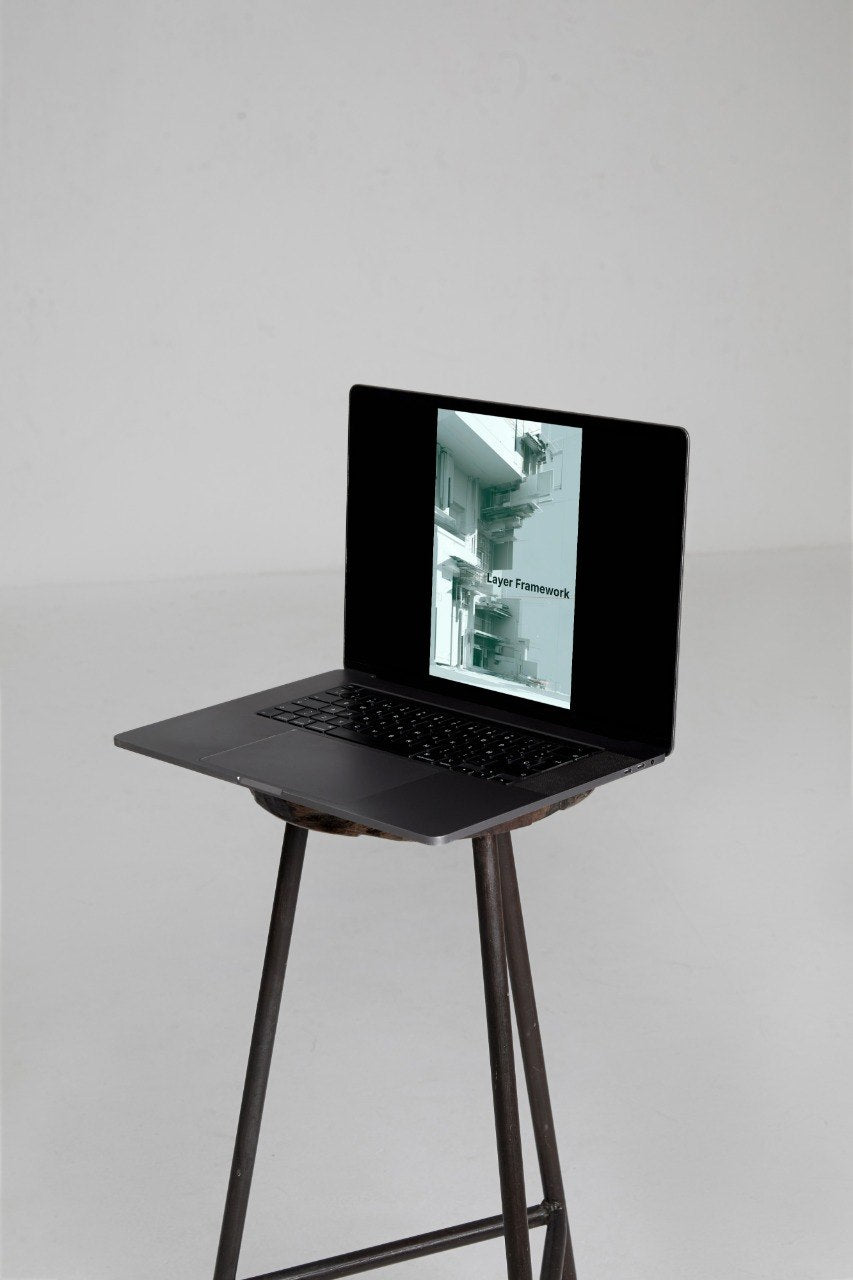 A black laptop with its screen open, displaying a grayscale architectural photograph, set on a dark metal tripod stand against a light gray studio background.