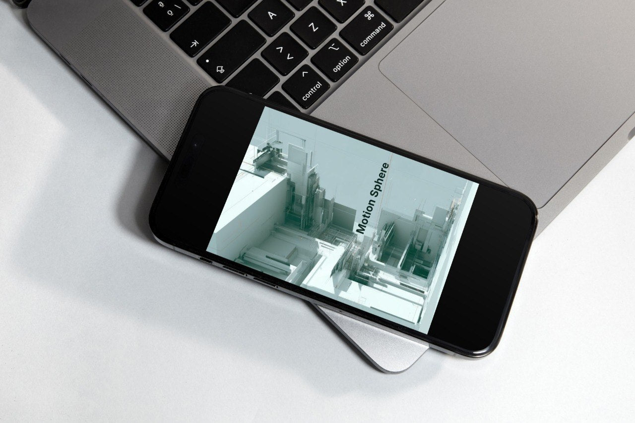 A black smartphone lying diagonally across a silver laptop on a white surface, displaying a green-tinted interface with the text 'Motion Software'.